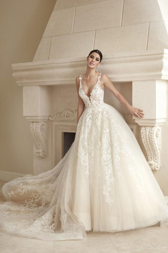 Bride in an ivory floral lace ballgown standing beside an ornate fireplace
